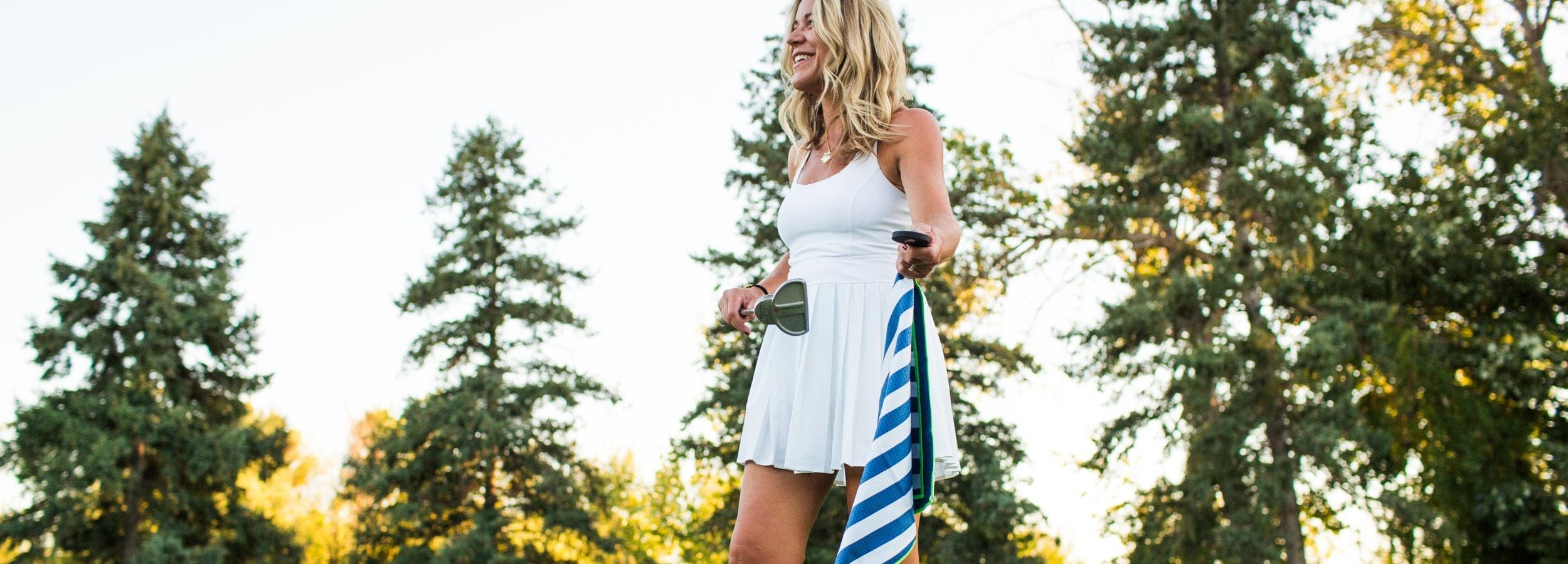 Woman in a white dress holding a blue and white striped bag with trees in the background