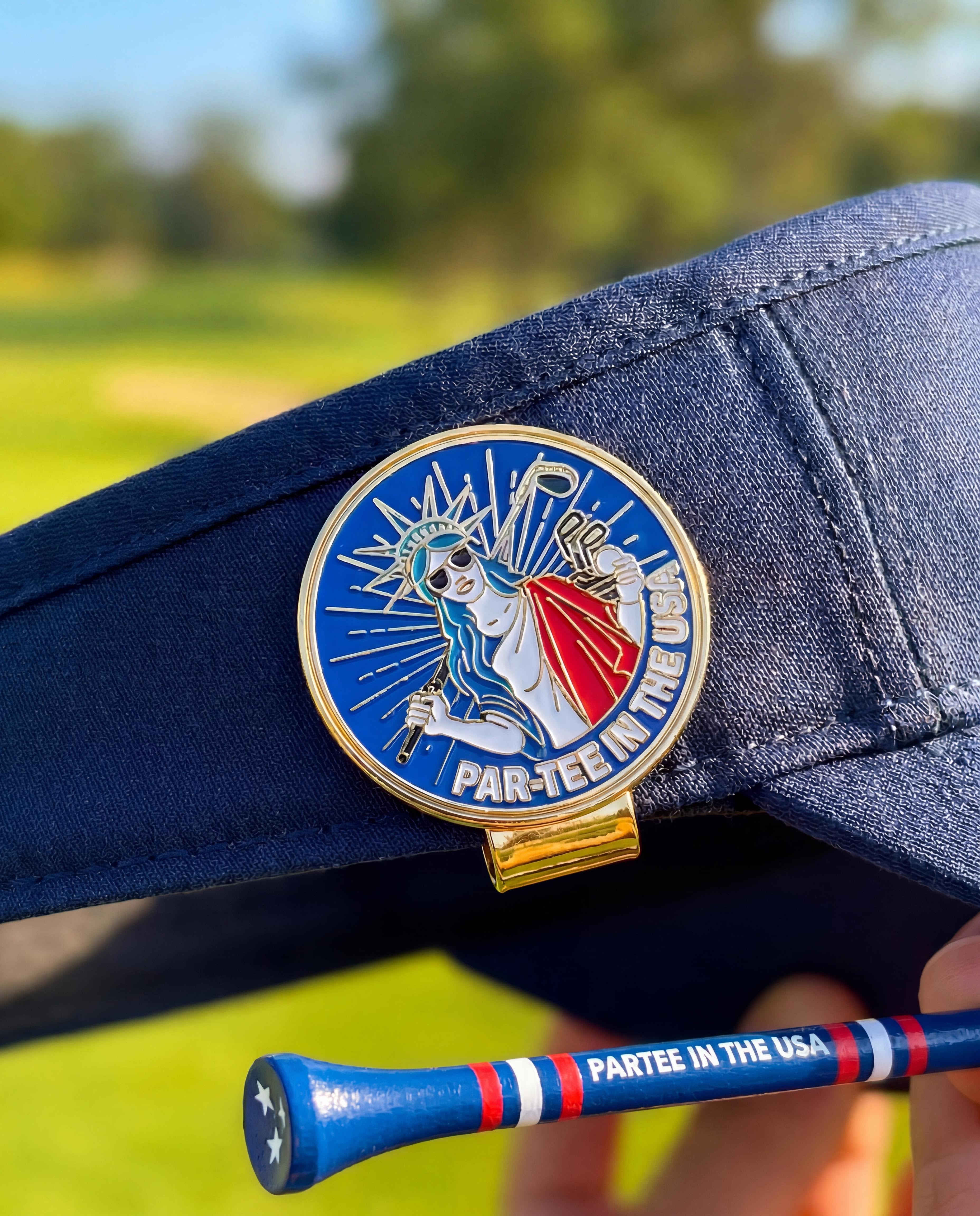 Navy blue cap with a 'Par-Tee in the USA' ball marker and a golf tee on a blurred green background