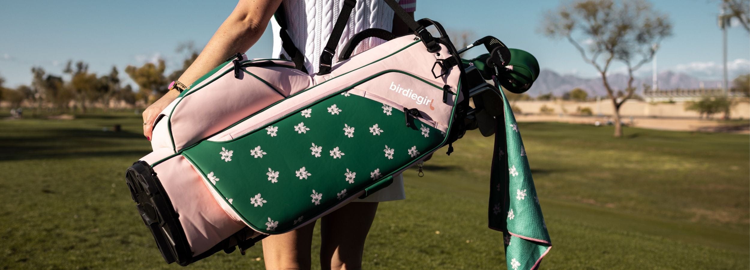 Woman  holding a golf bag with a green and pink design on a golf course