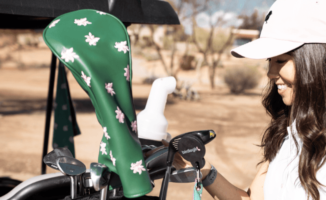 Woman holding a golf club with a green floral-patterned golf bag in the background