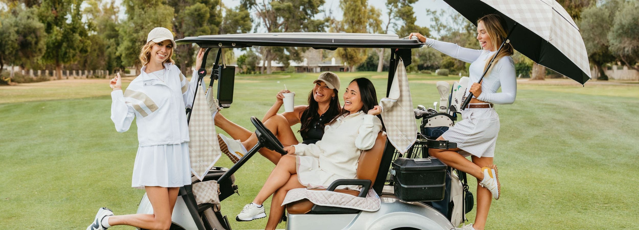 Four women in golf attire sitting in a golf cart on a golf course.