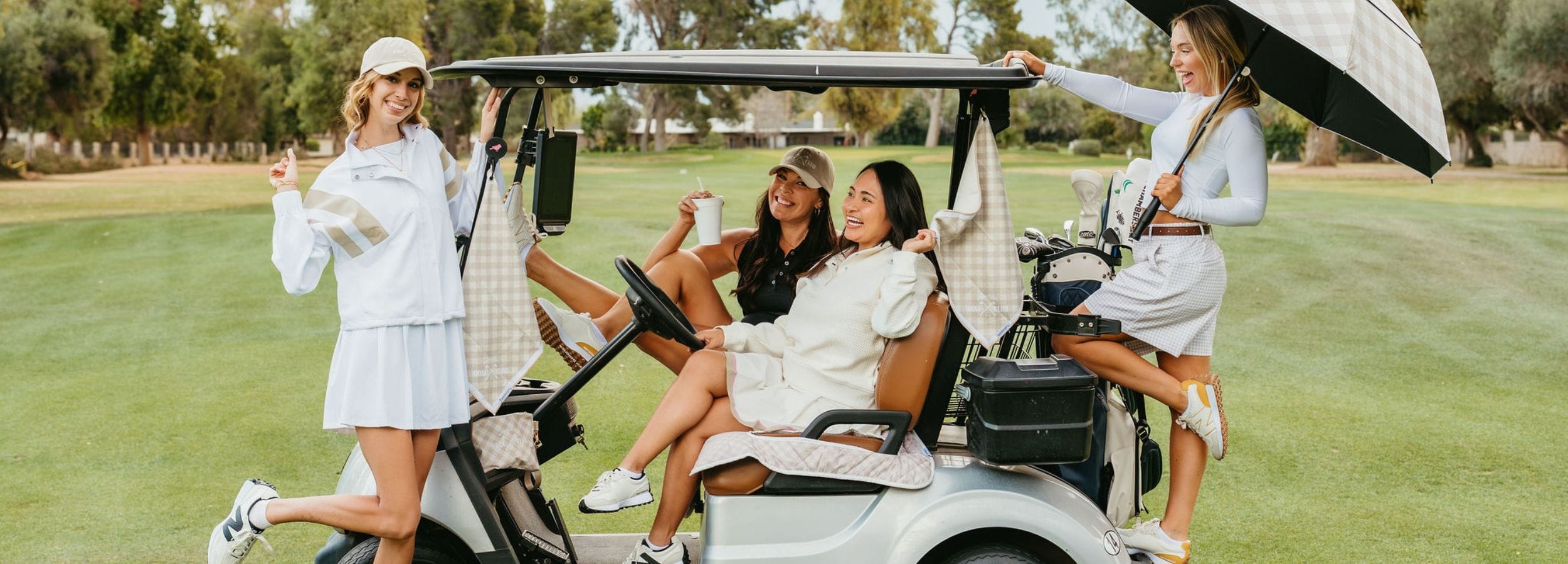 four women on a golf course with a golf cart seat cover and umbrella